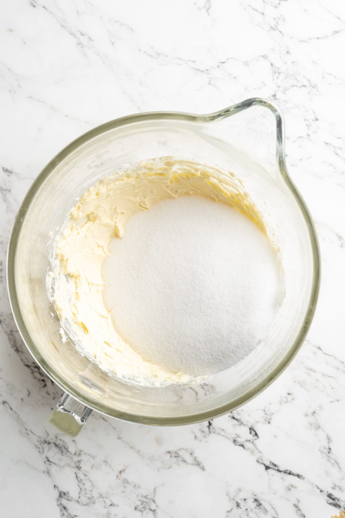 Granulated sugar and butter in a stand mixer bowl on white countertop