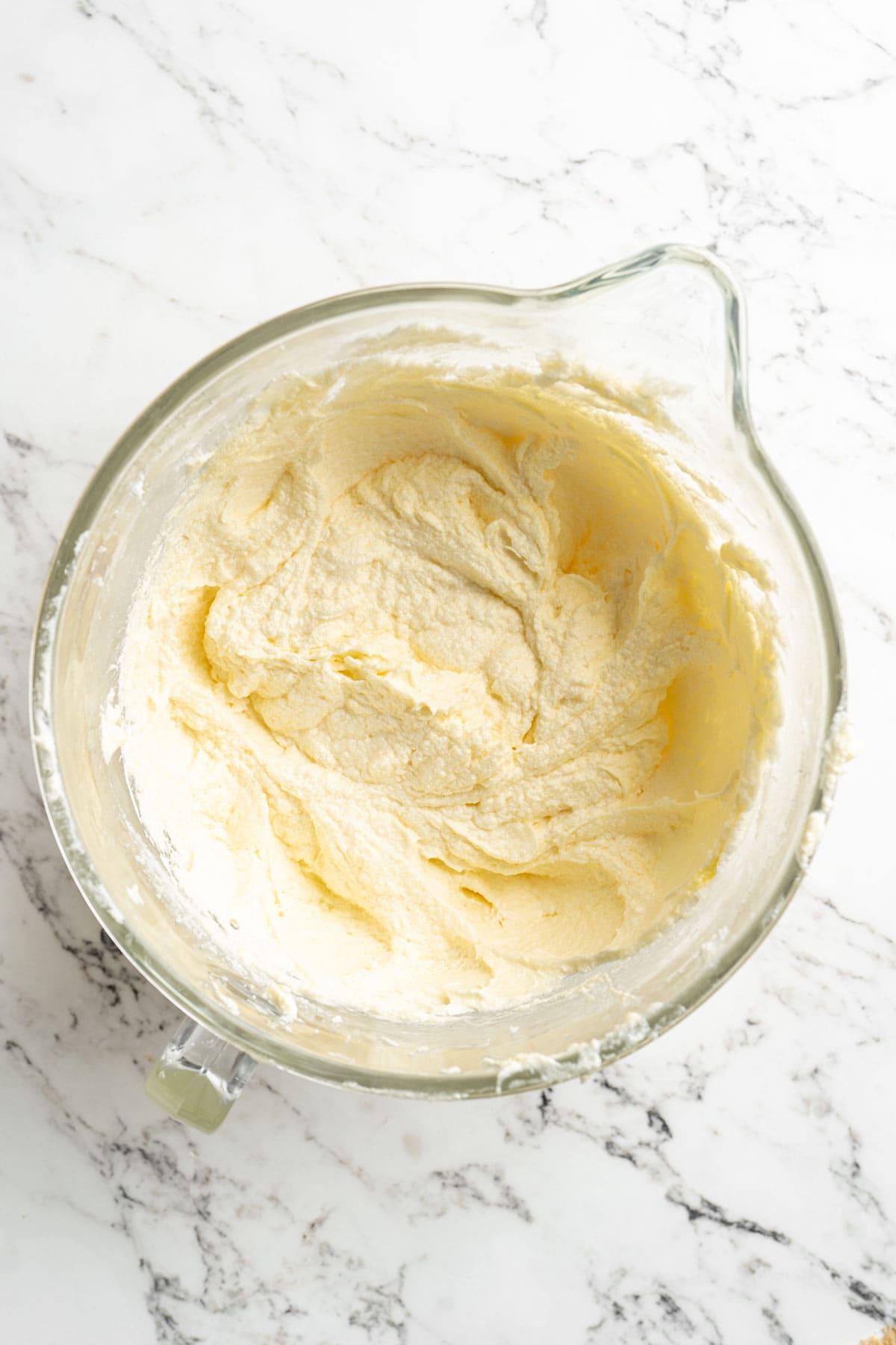 Creamed butter, sugar and eggs in a stand mixer bowl on white countertop