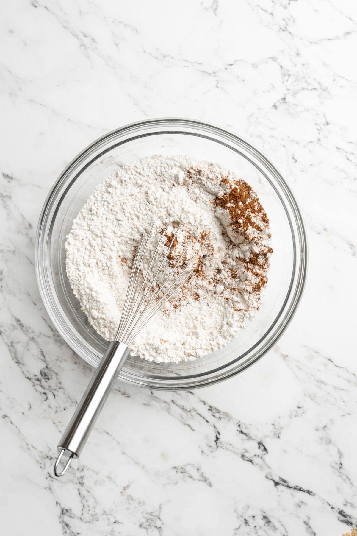 Flour and spices added to a glass bowl with a whisk on white countertop