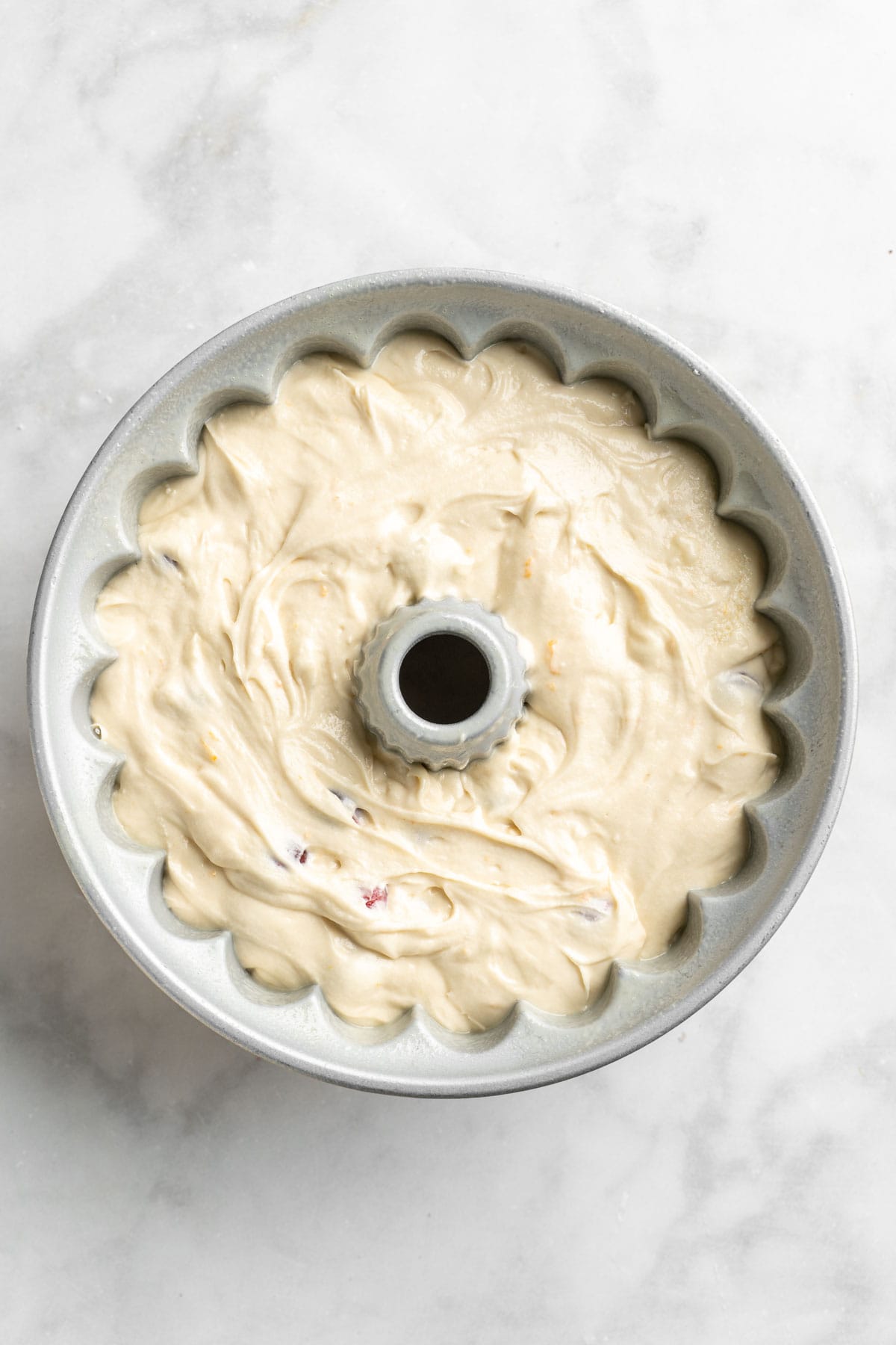 Cranberry orange bundt cake batter in a bundt pan on white countertop