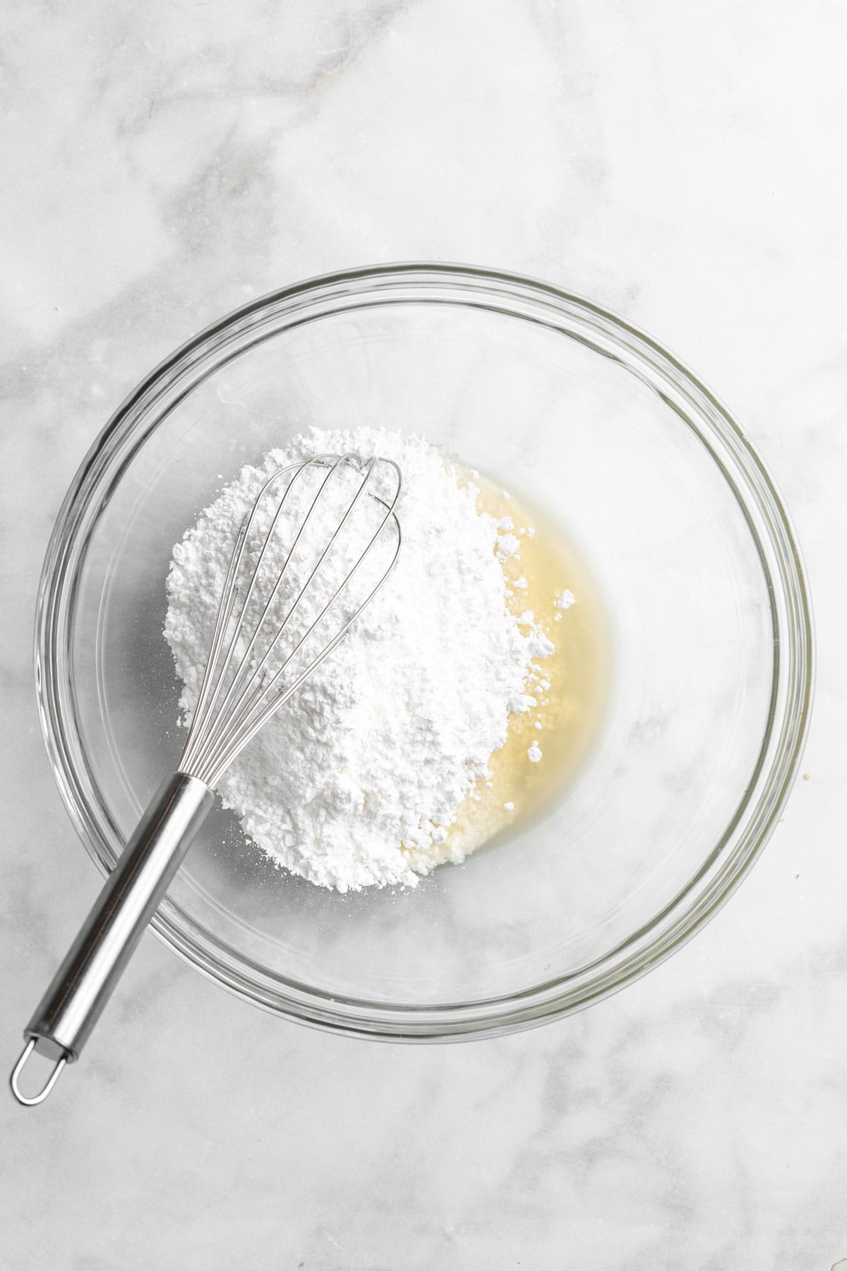 Orange juice and powdered sugar in a glass bowl being whisked together