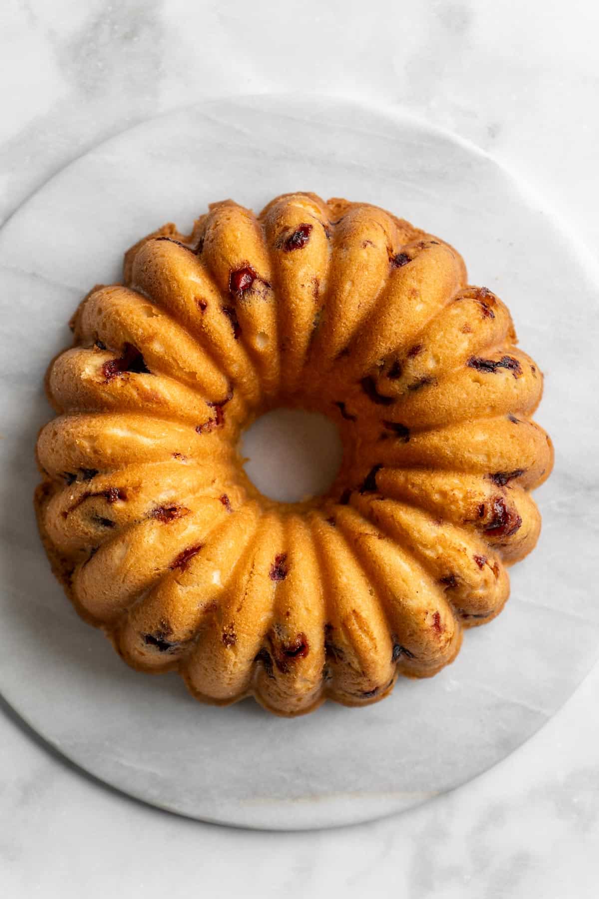 Inverted baked cranberry orange cake on platter on white background