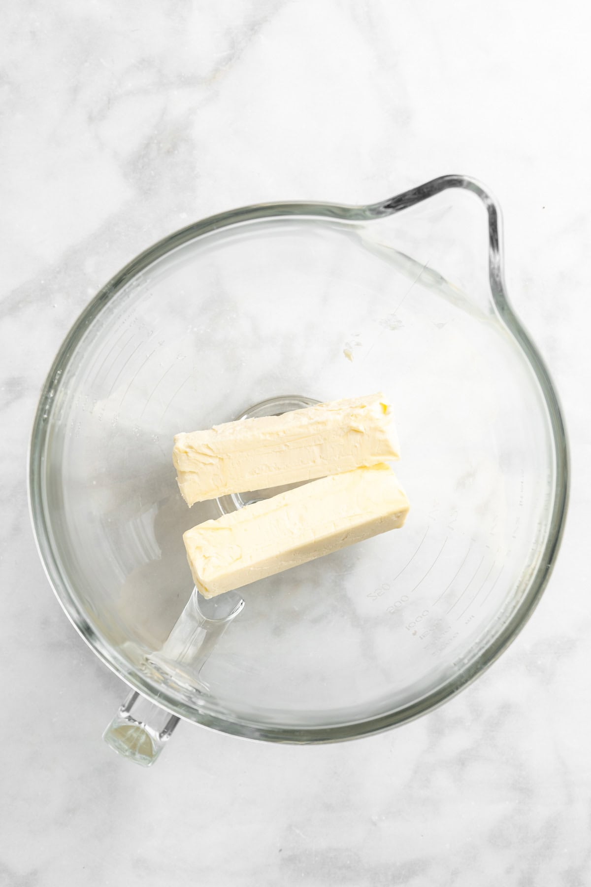 Softened butter in a glass mixing bowl on white countertop