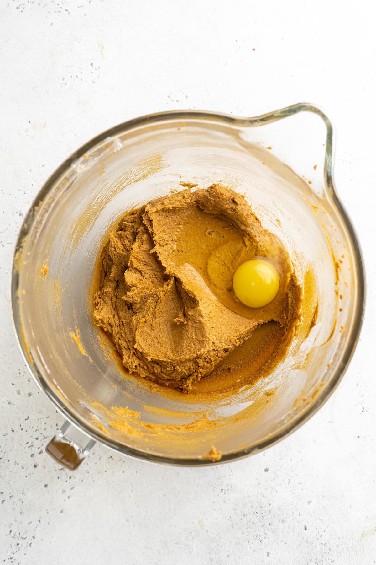 A mixing bowl containing thick gingerbread batter with an egg added on top, ready to be mixed