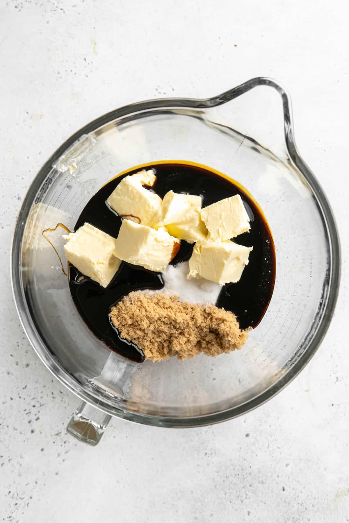 A glass mixing bowl with softened butter, brown sugar, and molasses, ready to be creamed together