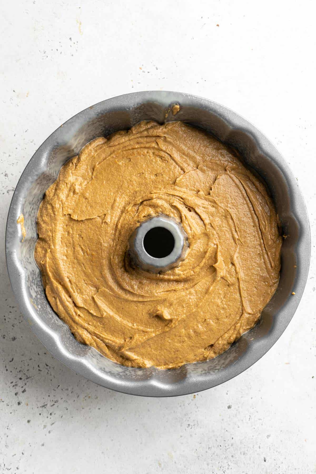 A greased Bundt pan filled with gingerbread batter, evenly spread and ready to bake