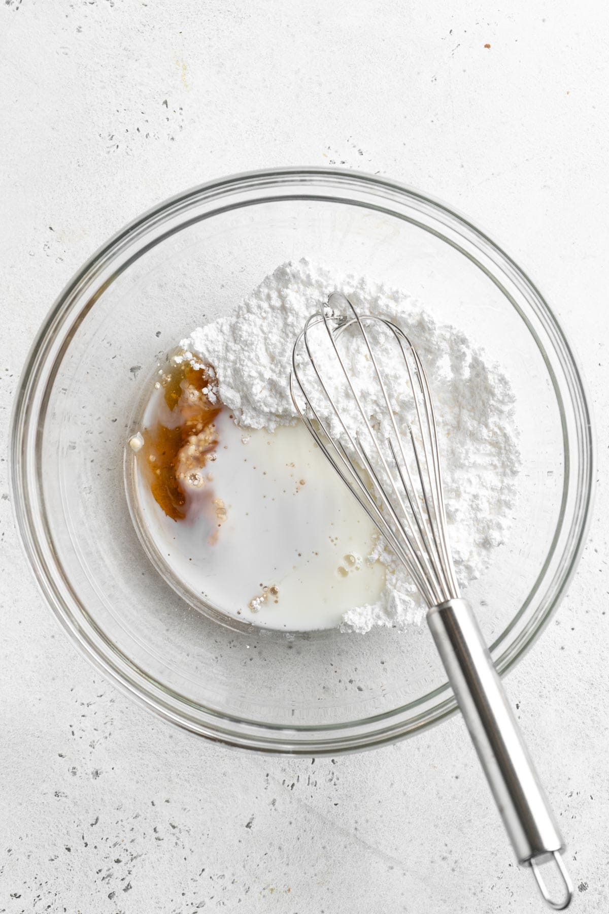 A glass bowl with powdered sugar, milk, and vanilla extract for icing, ready to be whisked