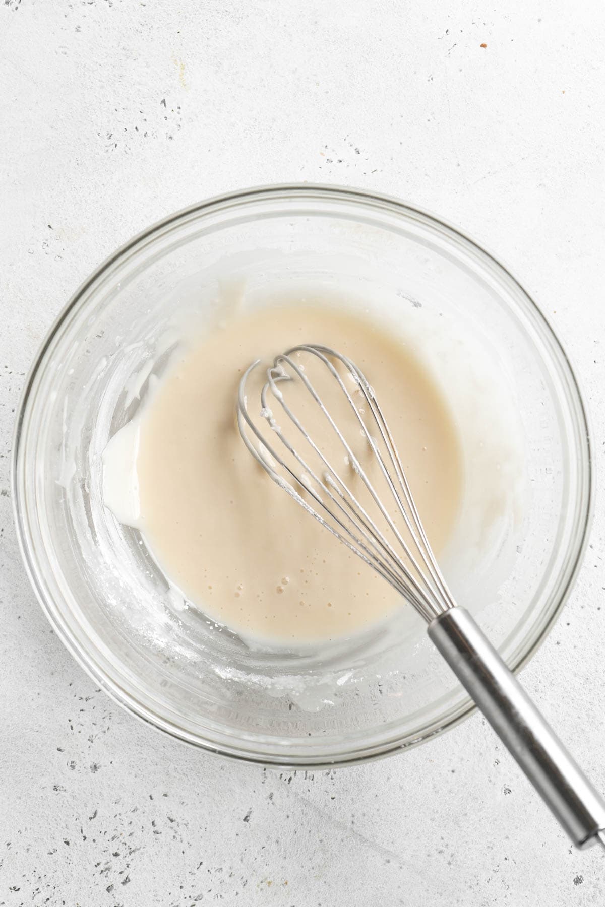 A glass bowl with smooth white icing fully mixed and ready for drizzling