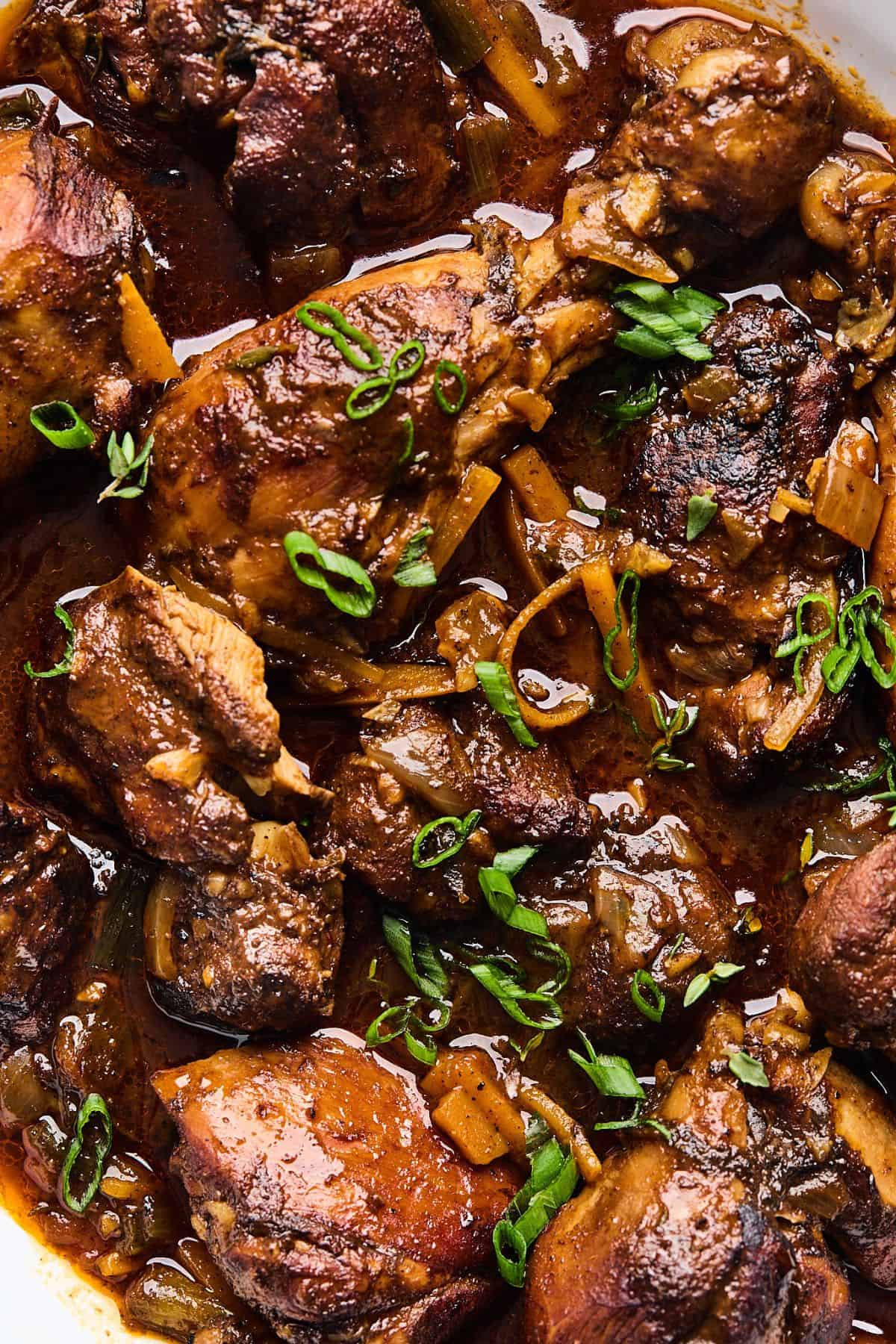 Close up of saucy jamaican brown stew chicken garnished with chopped scallions
