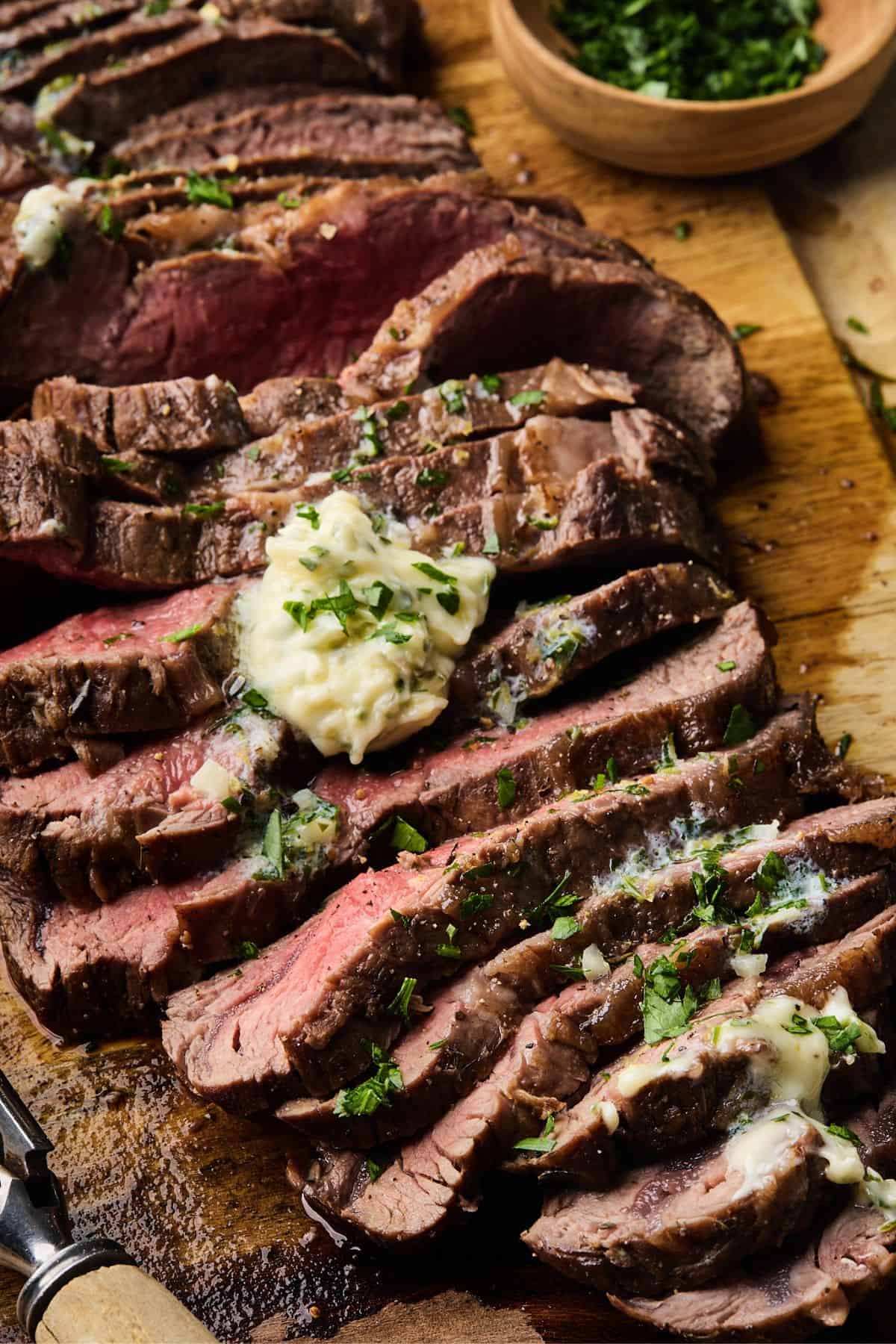Close up of london broil on a wooden cutting board sliced and smothered with herb butter