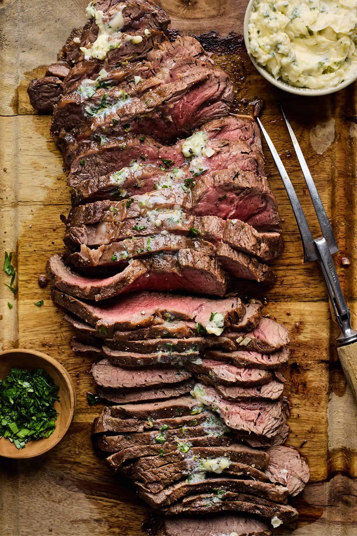 London broil smothered with herb butter on a wooden cutting board butter after slicing