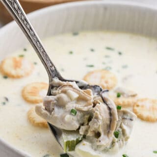 A delicious white bowl filled with oyster stew and a spoon digging in