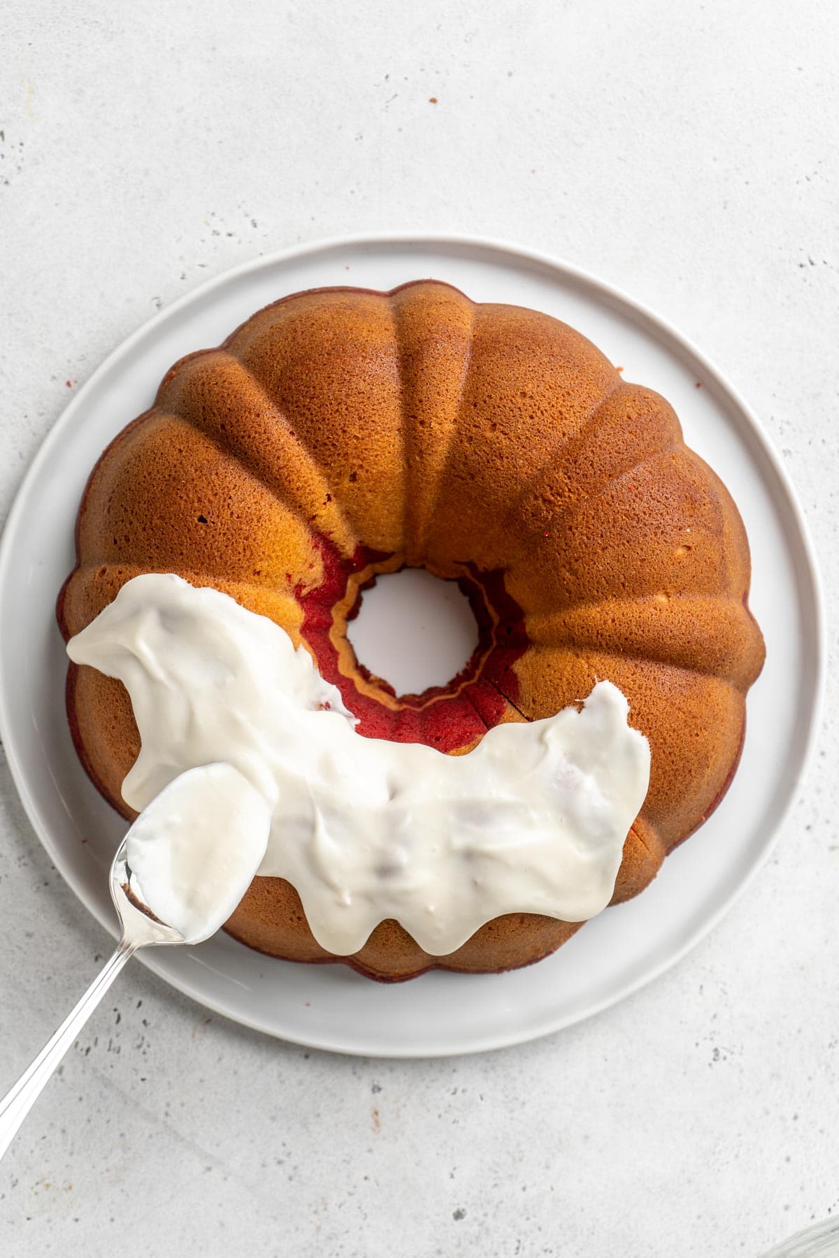 Cream cheese icing being spread over top of red velvet marble pound cake