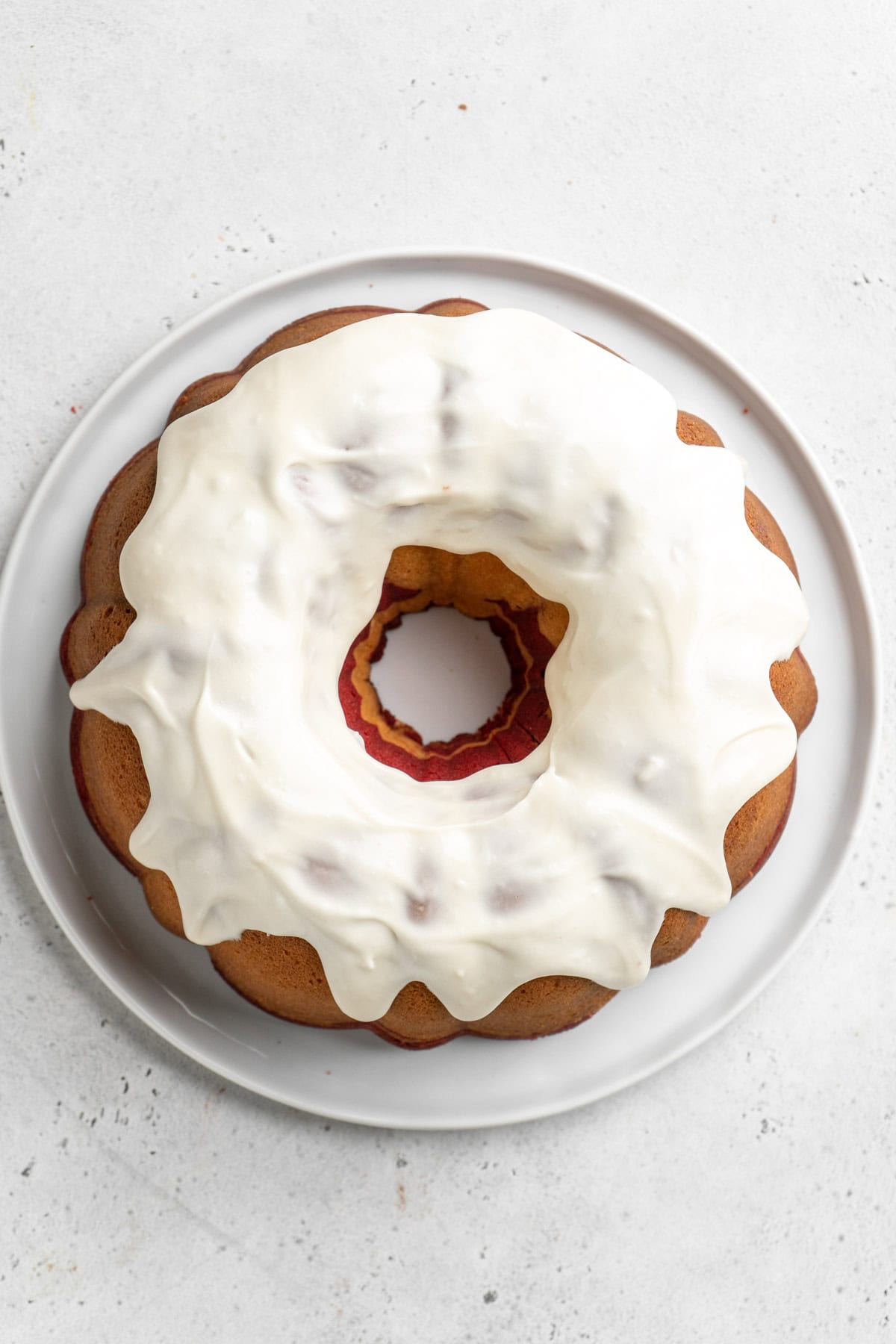 Spread cream cheese icing on top of bundt on white countertop