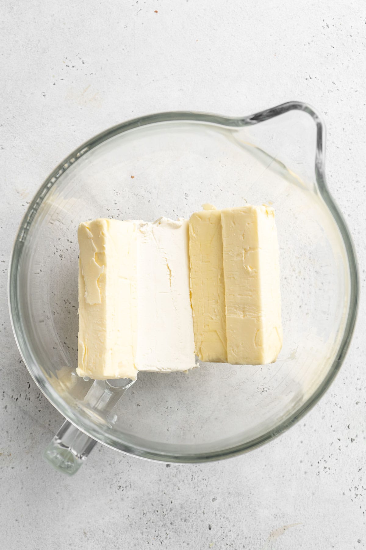 Butter and cream cheese in a glass mixer bowl on white countertop