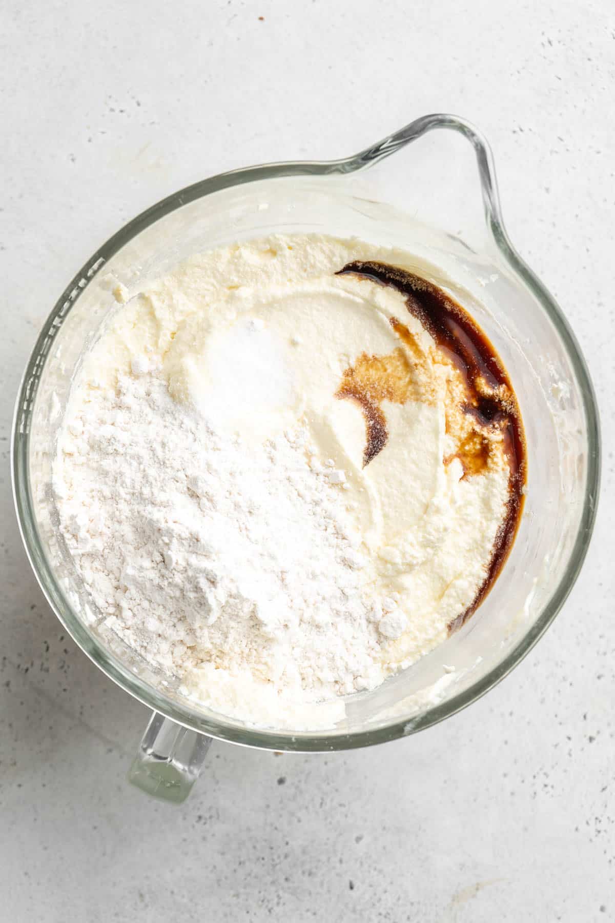 Flour and vanilla extract added to cake batter in glass bowl on white countertop