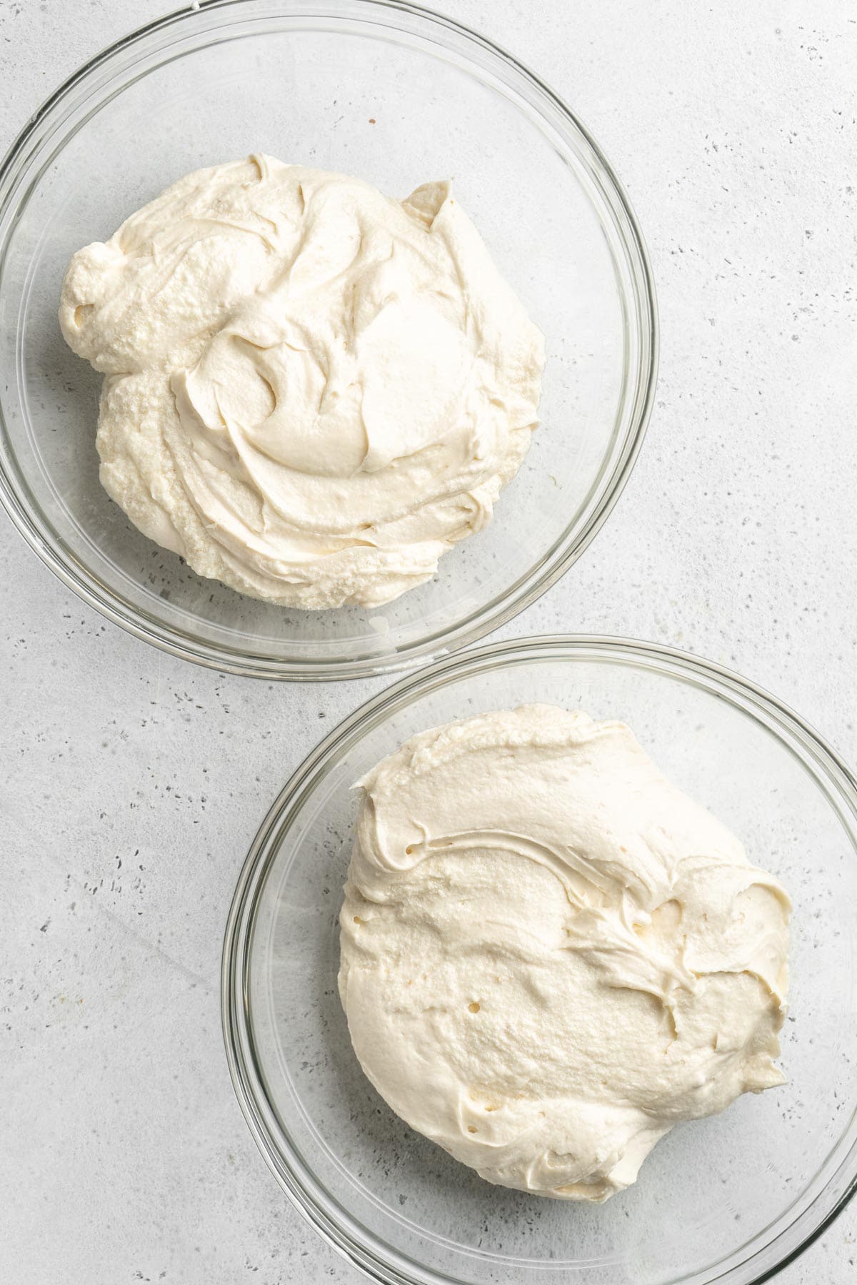 Cake batter divided into two separate glass bowls on white countertop