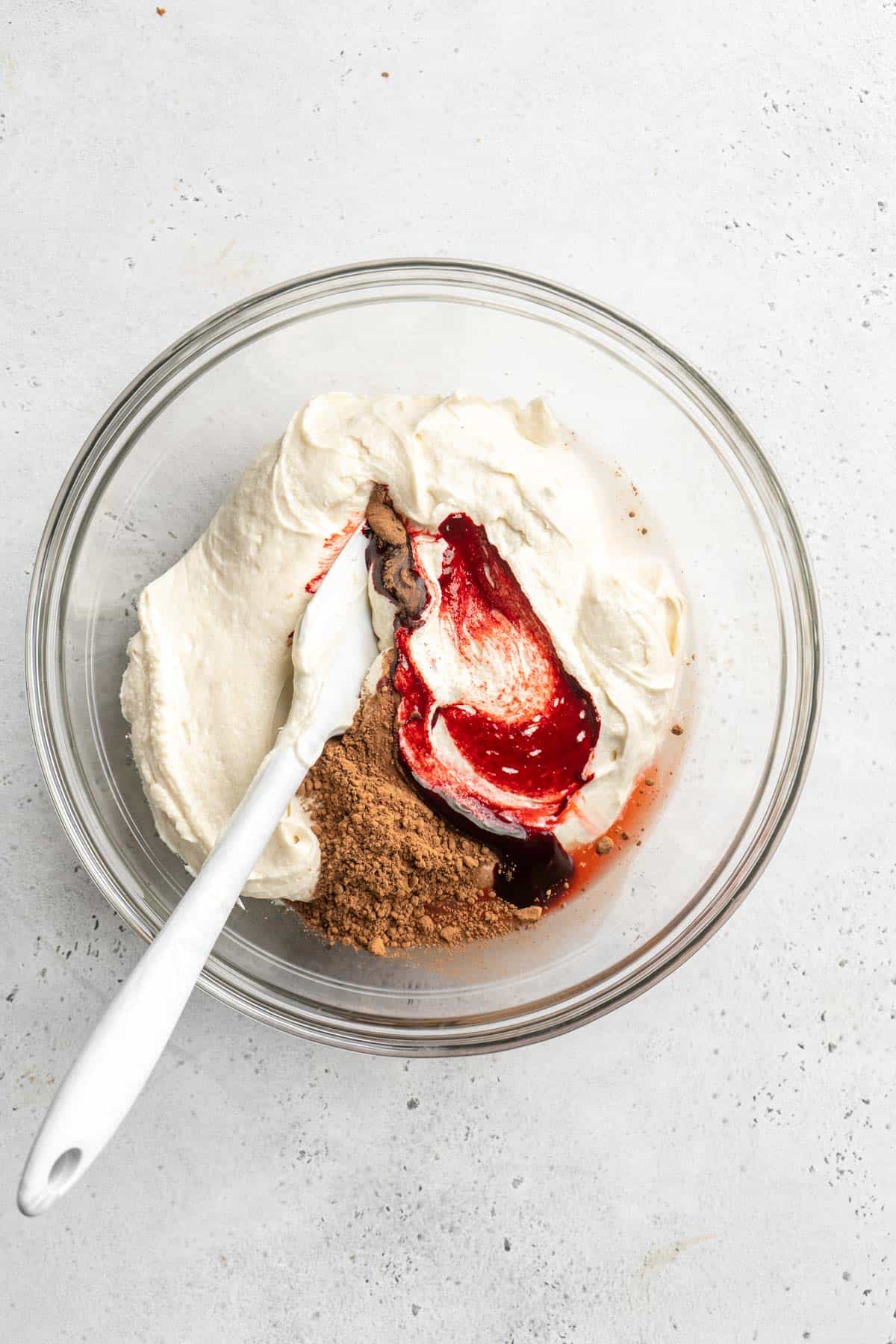 Red food coloring and cocoa powder added to a glass bowl mixing together