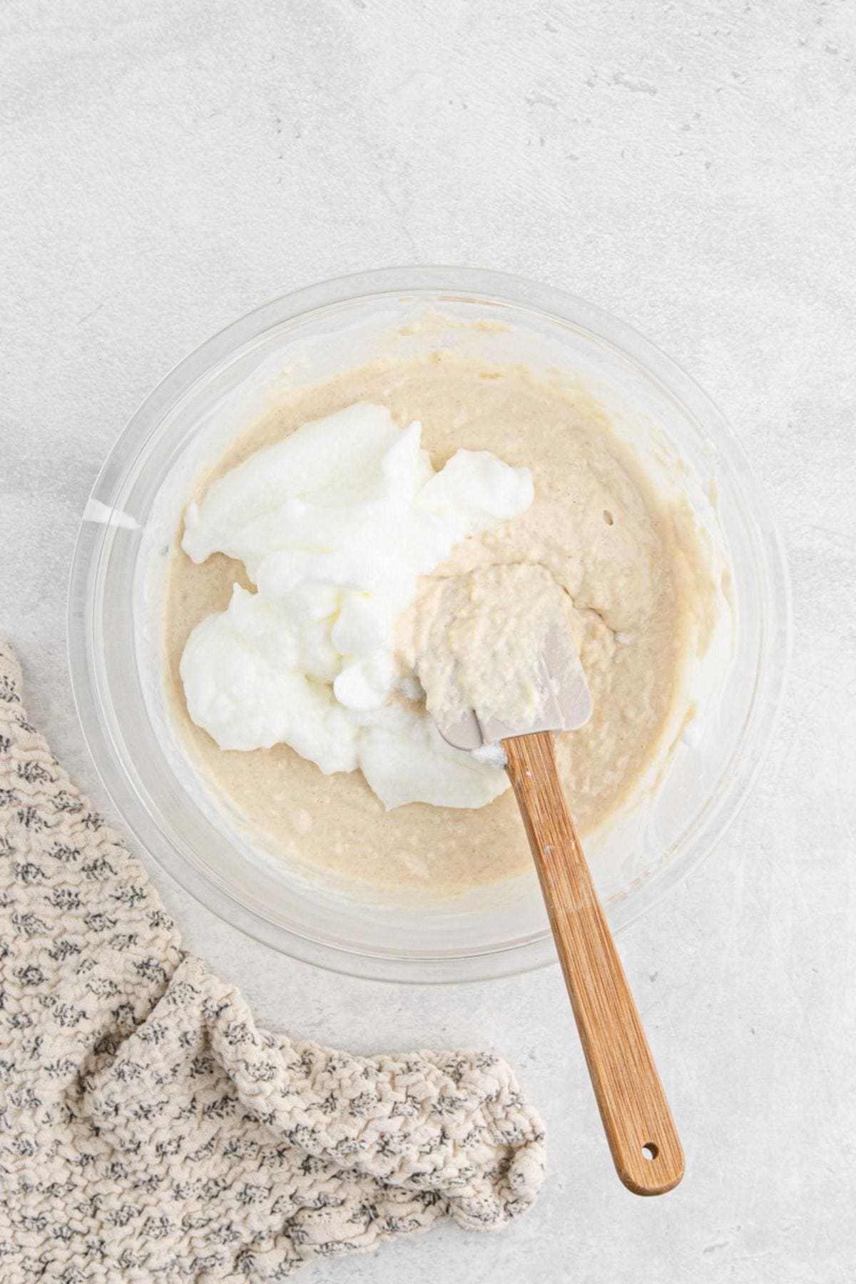 Batter in a bowl with whipped egg whites being folded in using a spatula