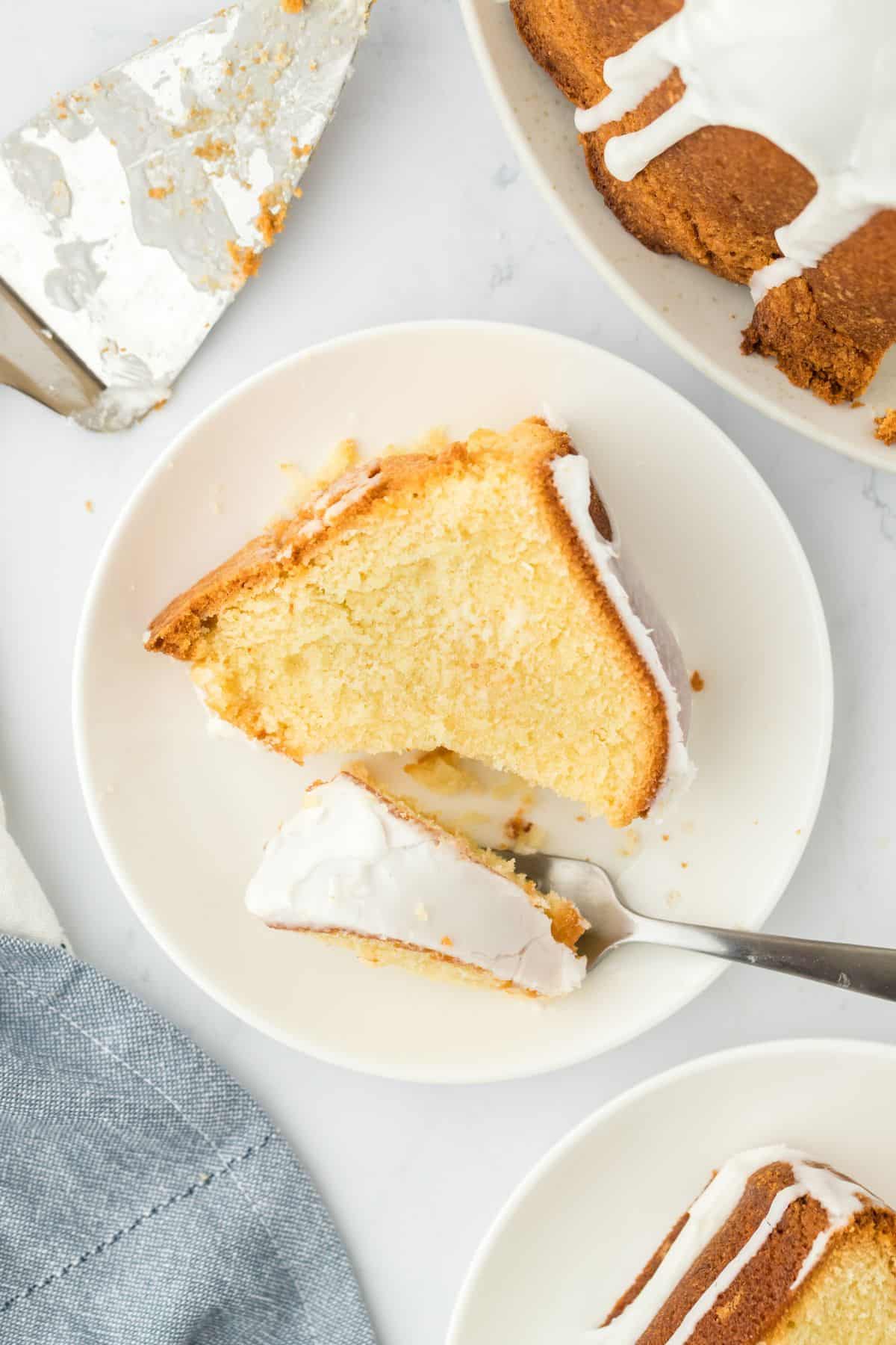 Overhead shot of a slice of million dollar pound cake with creamy white glaze, resting on a white plate with a portion of the slice on a fork next to it