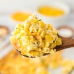 a scoop of scalloped corn coming out of a glass container