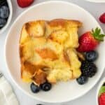 Overhead shot of a piece of white chocolate bread pudding on a white plate garnished with fresh strawberries, blueberries, and blackberries