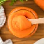Overhead shot of a jar filled with smooth carrot puree being scooped with a wooden spoon
