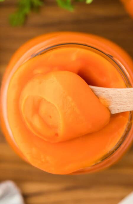 Overhead shot of a jar filled with smooth carrot puree being scooped with a wooden spoon