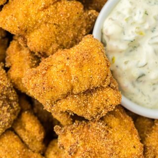 Closeup of crispy catfish nuggets stacked with a small bowl of creamy tartar sauce
