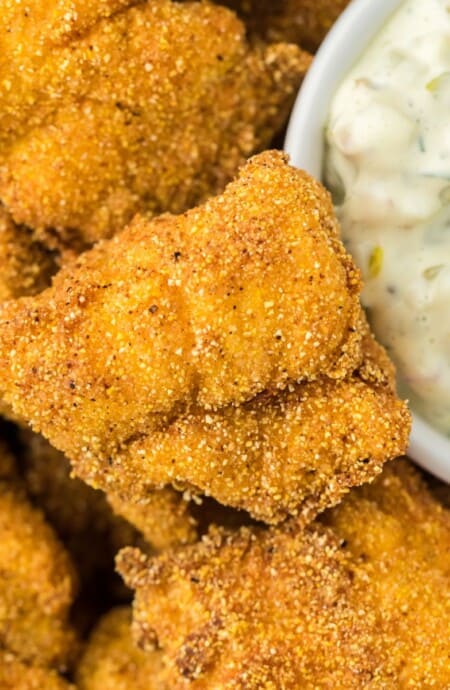 Closeup of crispy catfish nuggets stacked with a small bowl of creamy tartar sauce