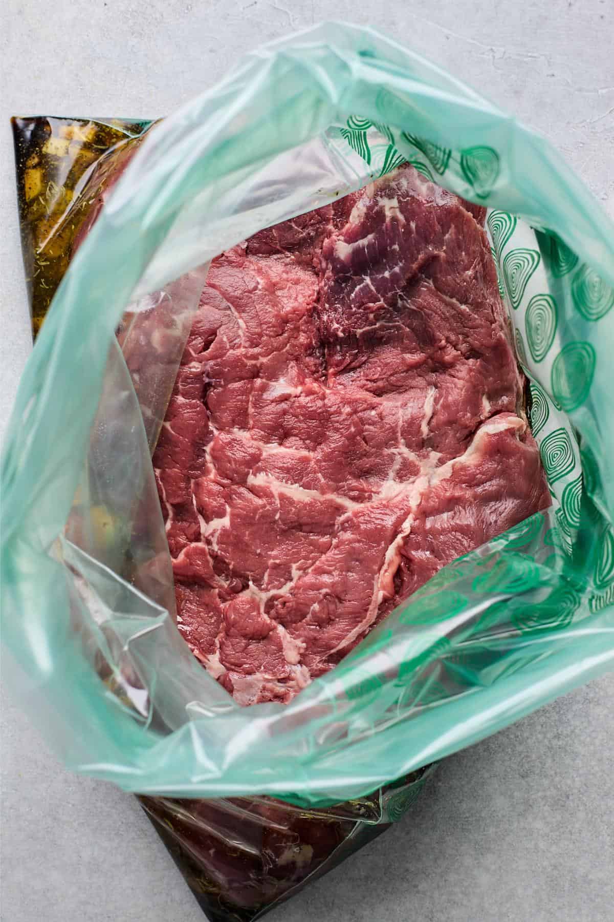 A raw steak placed inside a plastic bag filled with marinade