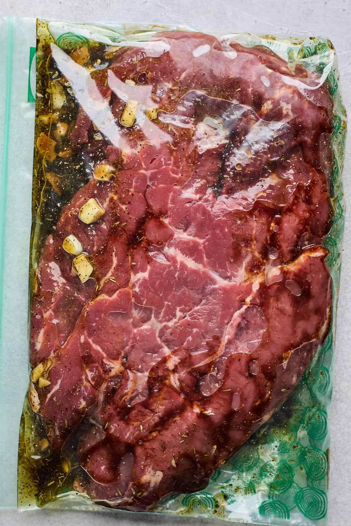 Meat marinating in a plastic bag with sliced garlic and seasonings