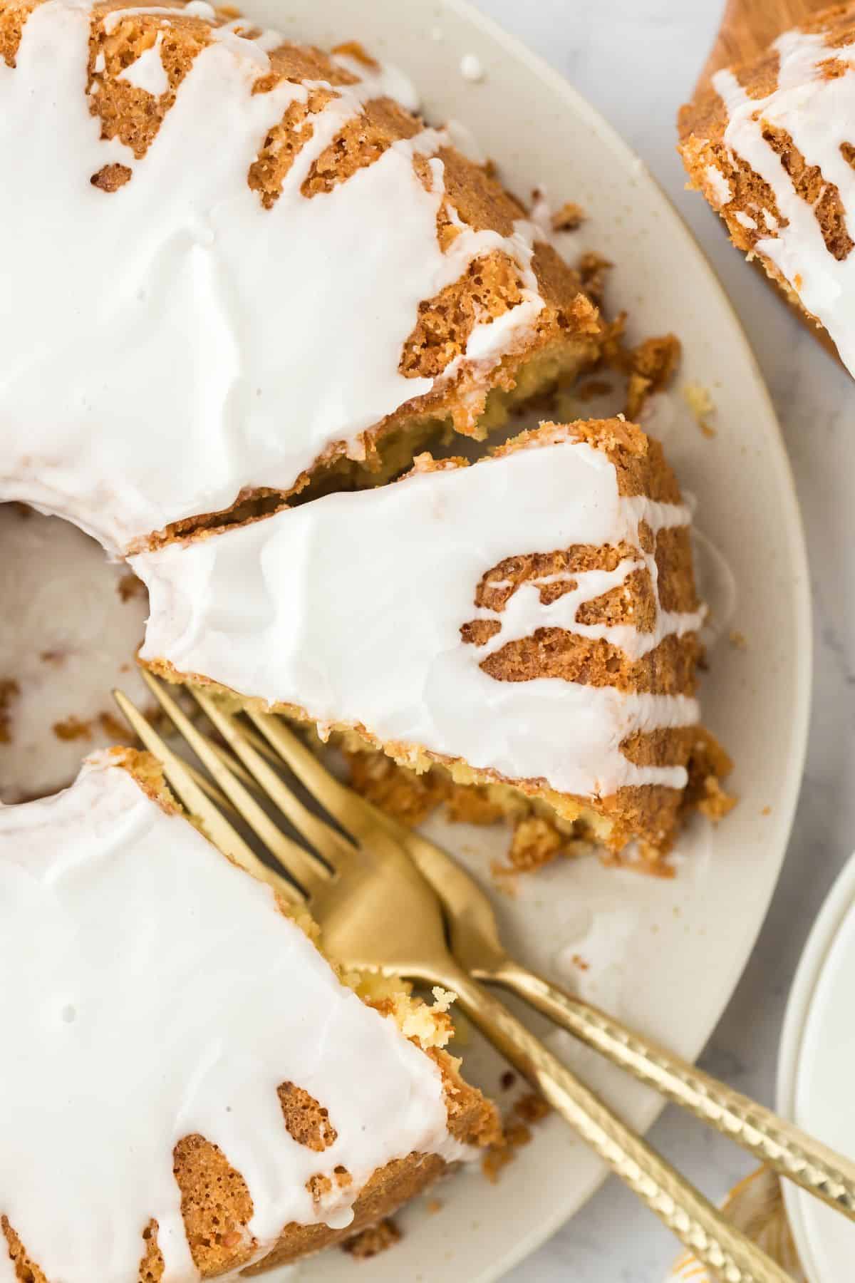 Overhead shot of Louisiana Crunch Cake with white glaze, placed on a plate with a slice being taken out, with golden forks next to it
