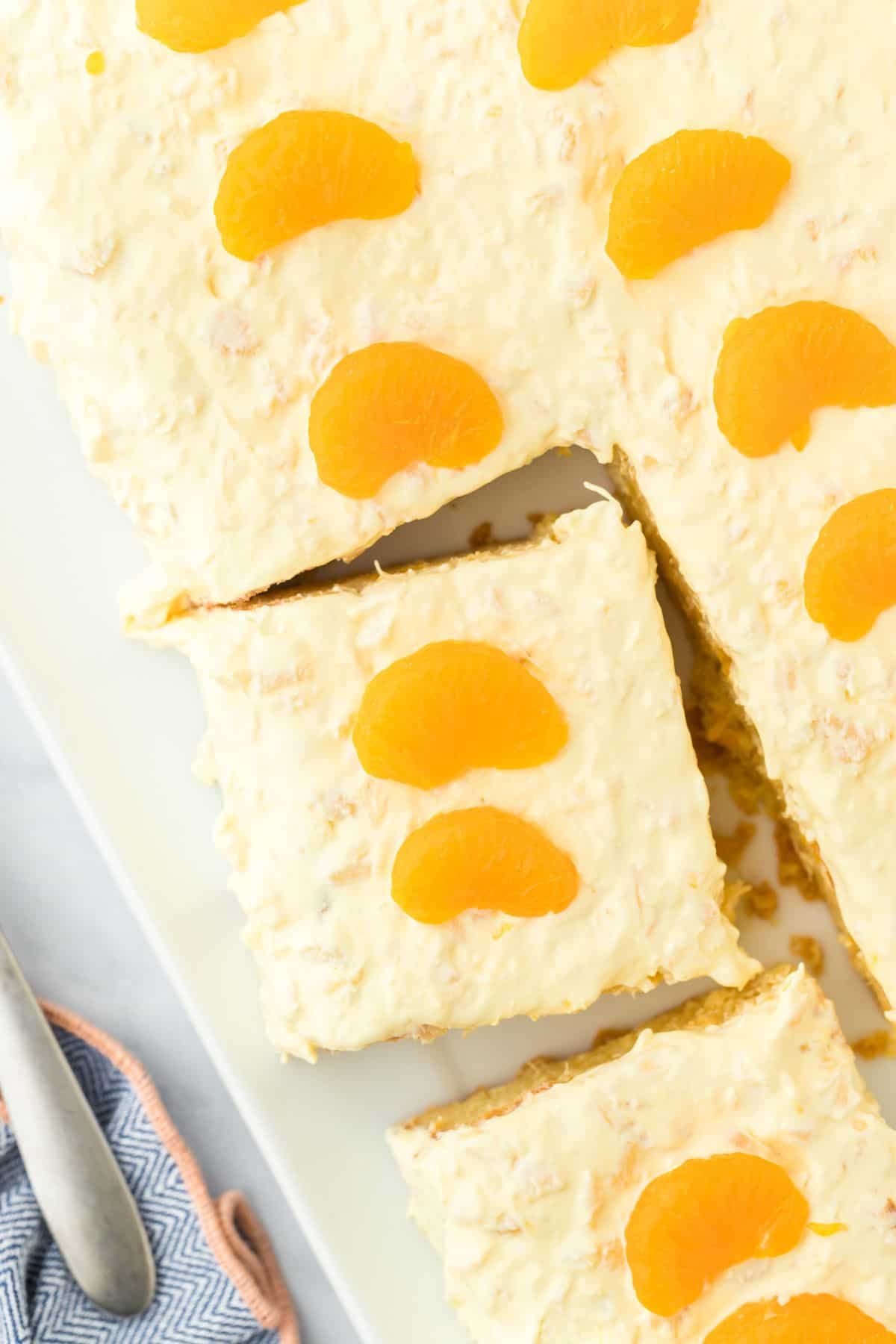 Overhead shot of pig pickin' cake topped with mandarin oranges, cut into squares