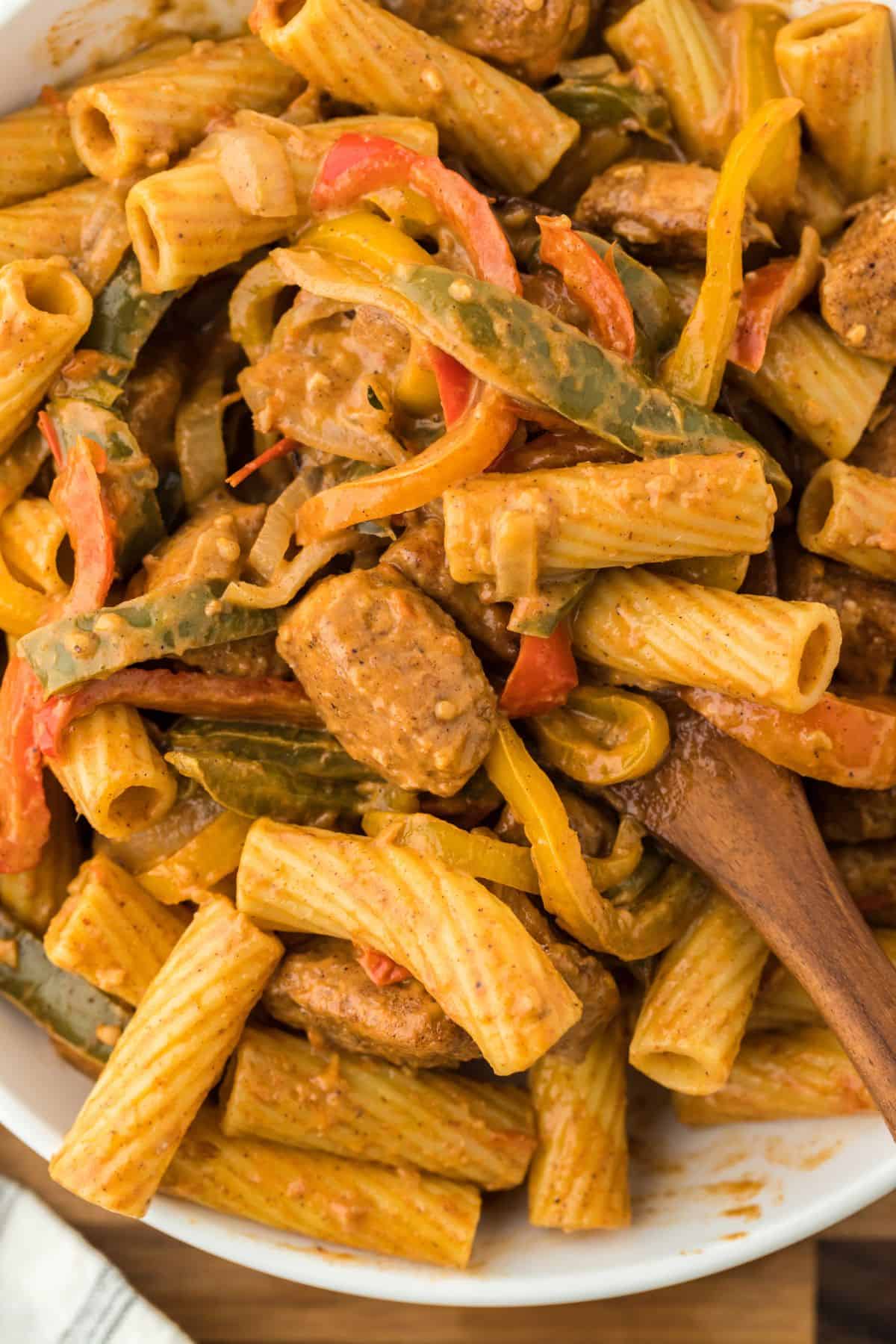 Closeup of of rasta pasta in a bowl with a wooden spoon stirring the pasta