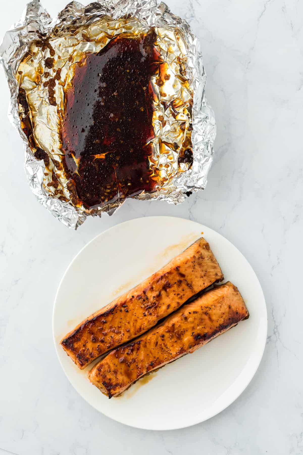 Finished salmon on a plate ith the leftover sauce visible in the foil next to it