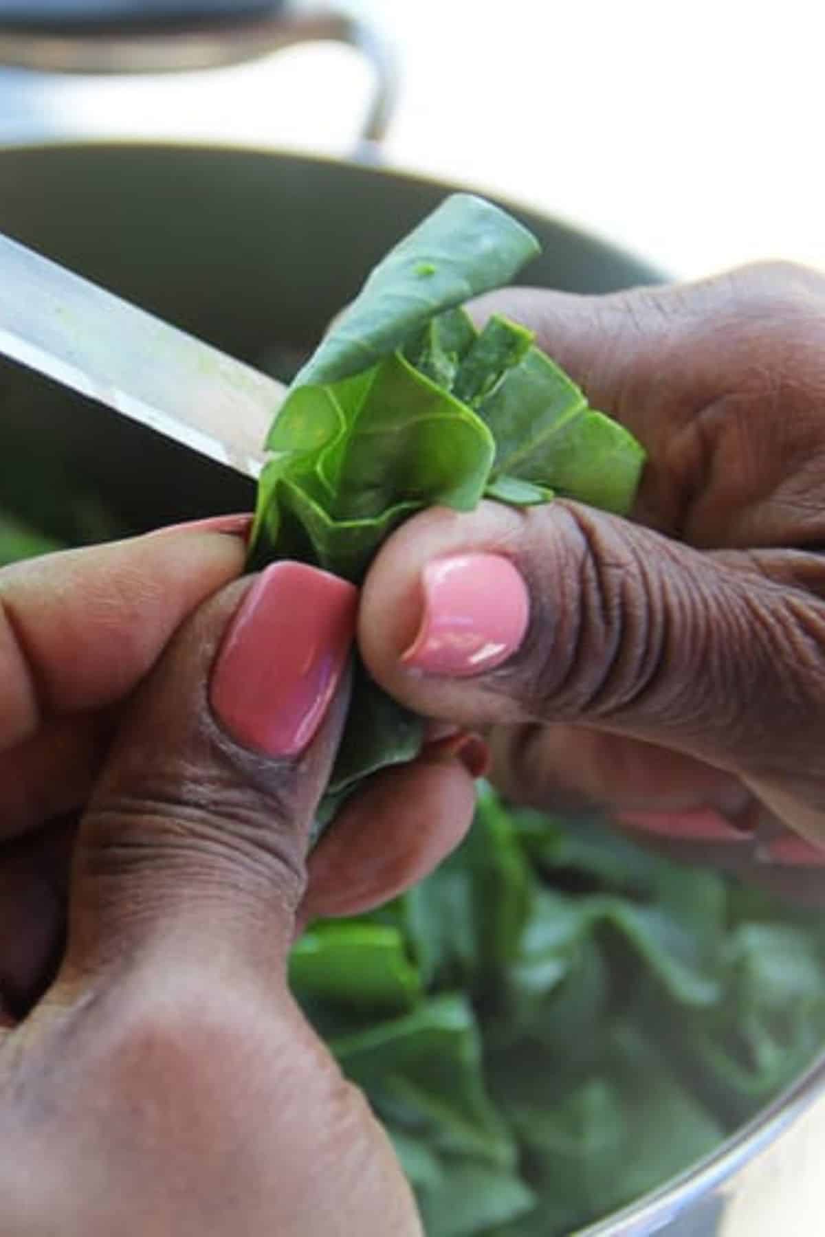 Hands with pink nails slicing collard greens with a small knife