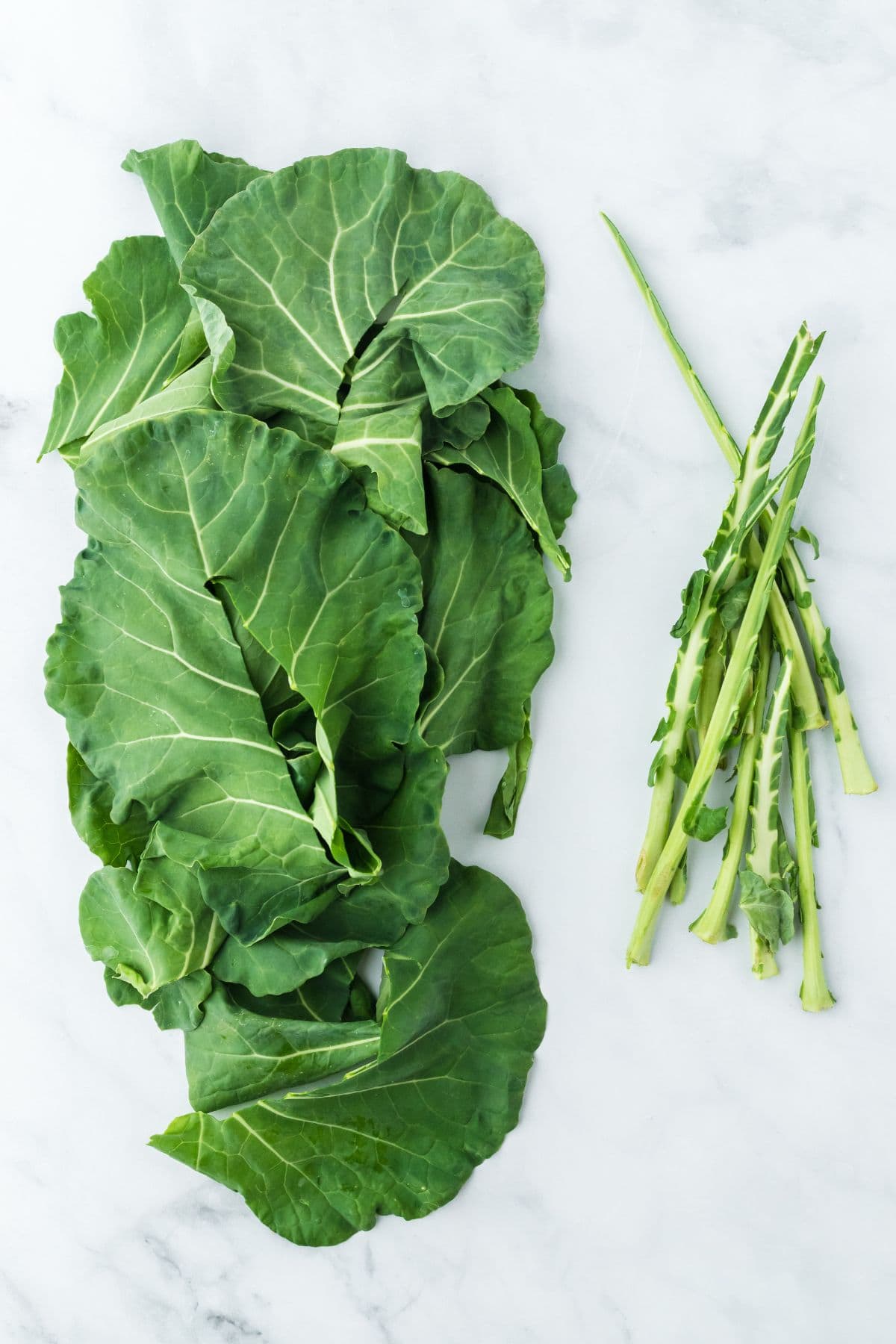 Fresh collard green leaves separated from their stems on a marble surface