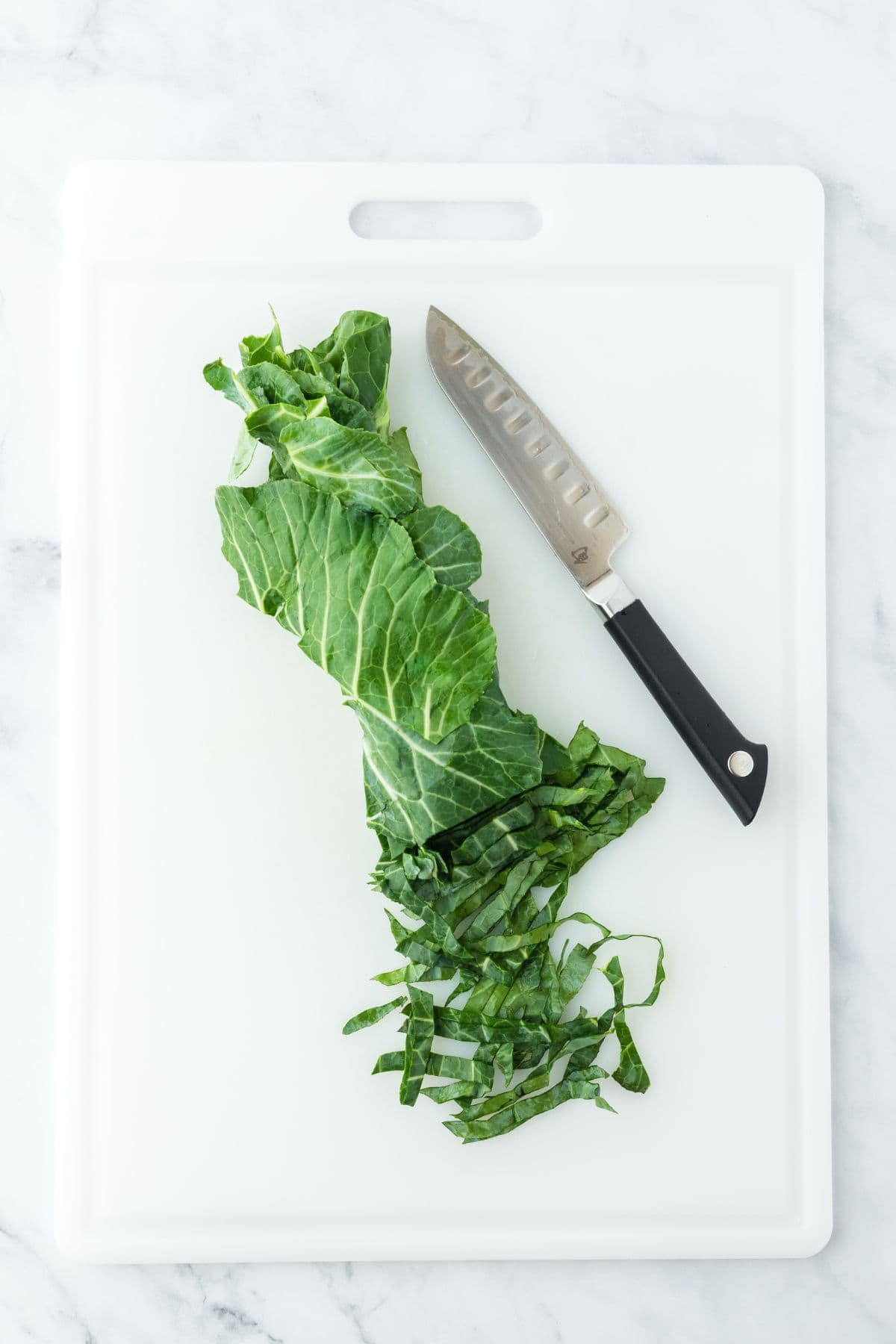 Collard greens rolled and sliced into thin strips on a white cutting board with a knife