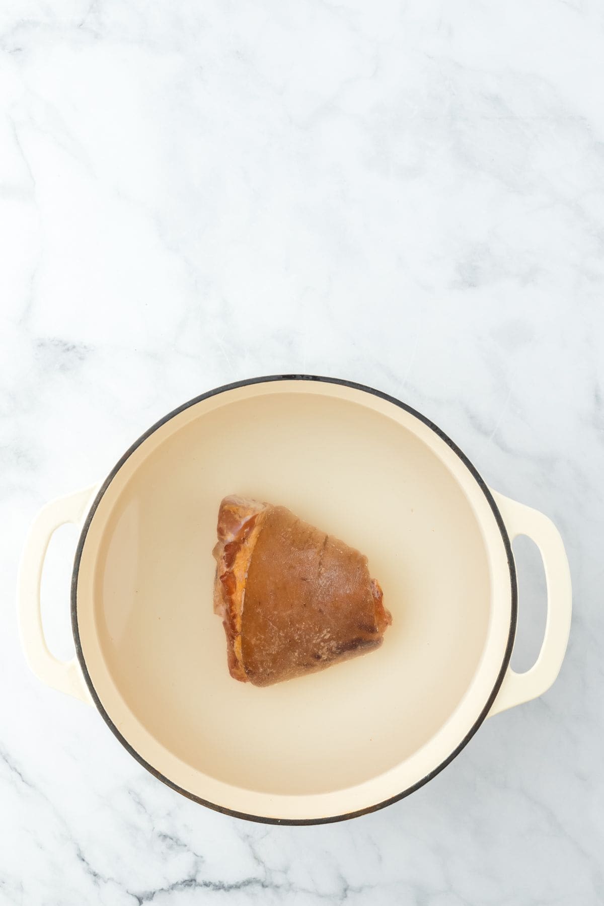 A smoked ham hock sitting in a large cream-colored pot