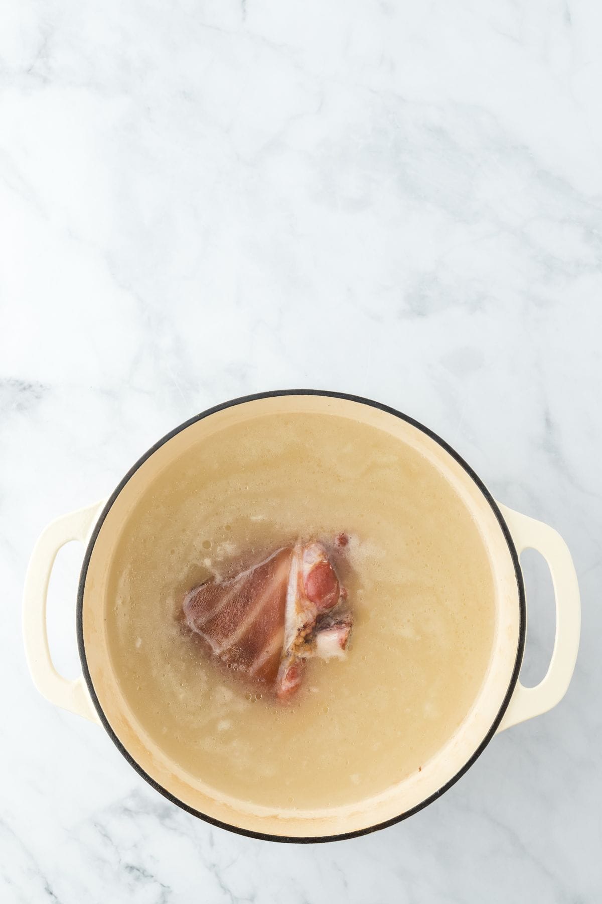 A smoked ham hock simmering in water in a Dutch oven