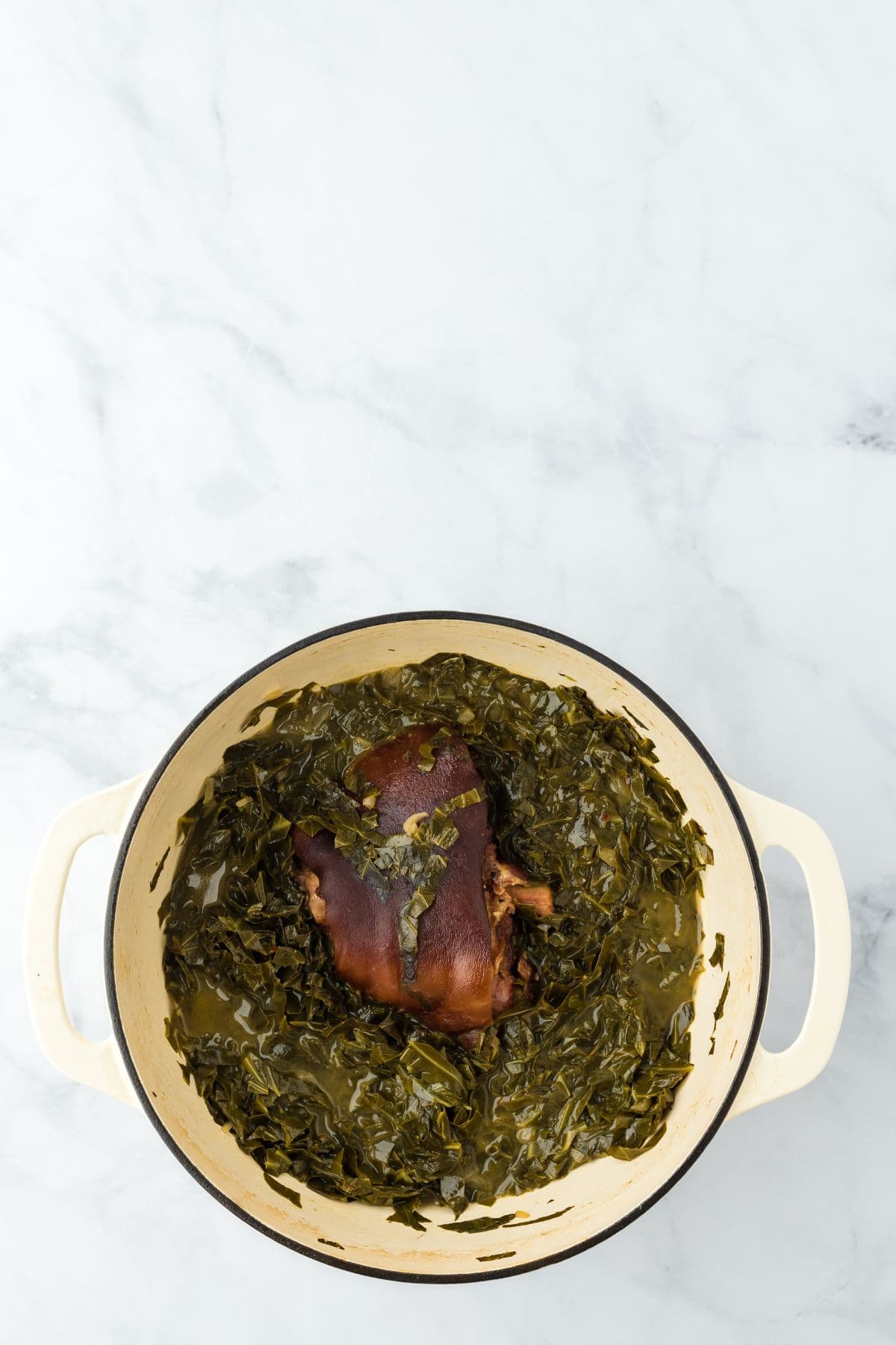 Fully cooked collard greens in a Dutch oven with a tender ham hock in the center