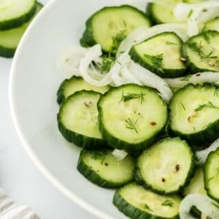 A white plate filled with cucumber and onion salad on a white background