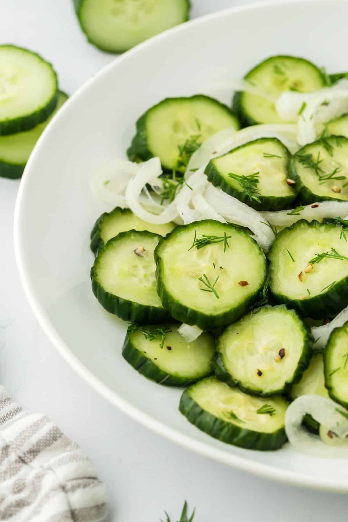 A white plate filled with cucumber and onion salad on a white background