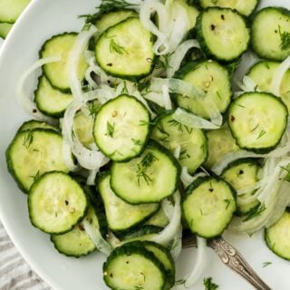 Overhead shot of cucumber and onion salad garnished with dill, arranged in a white plate