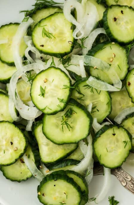 Overhead shot of cucumber and onion salad garnished with dill, arranged in a white plate