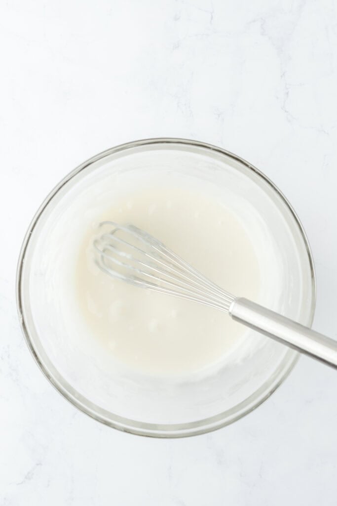 Whisked cake glaze in a white glass bowl on white countertop