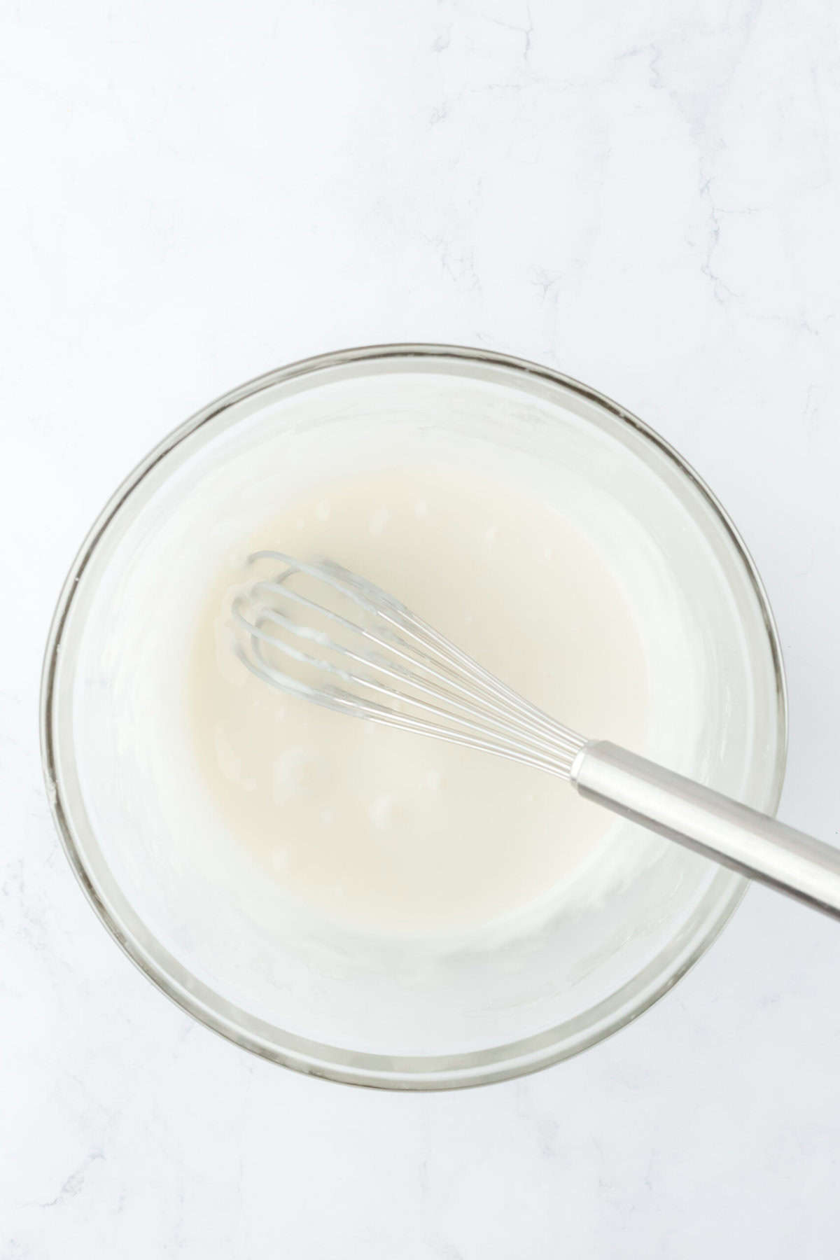 Whisked cake glaze in a white glass bowl on white countertop