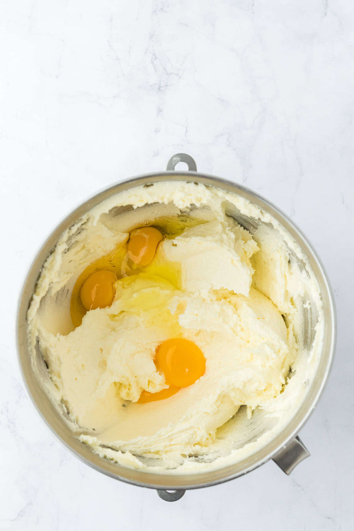 Eggs added to a stand mixer with creamed butter and sugar on white countertop