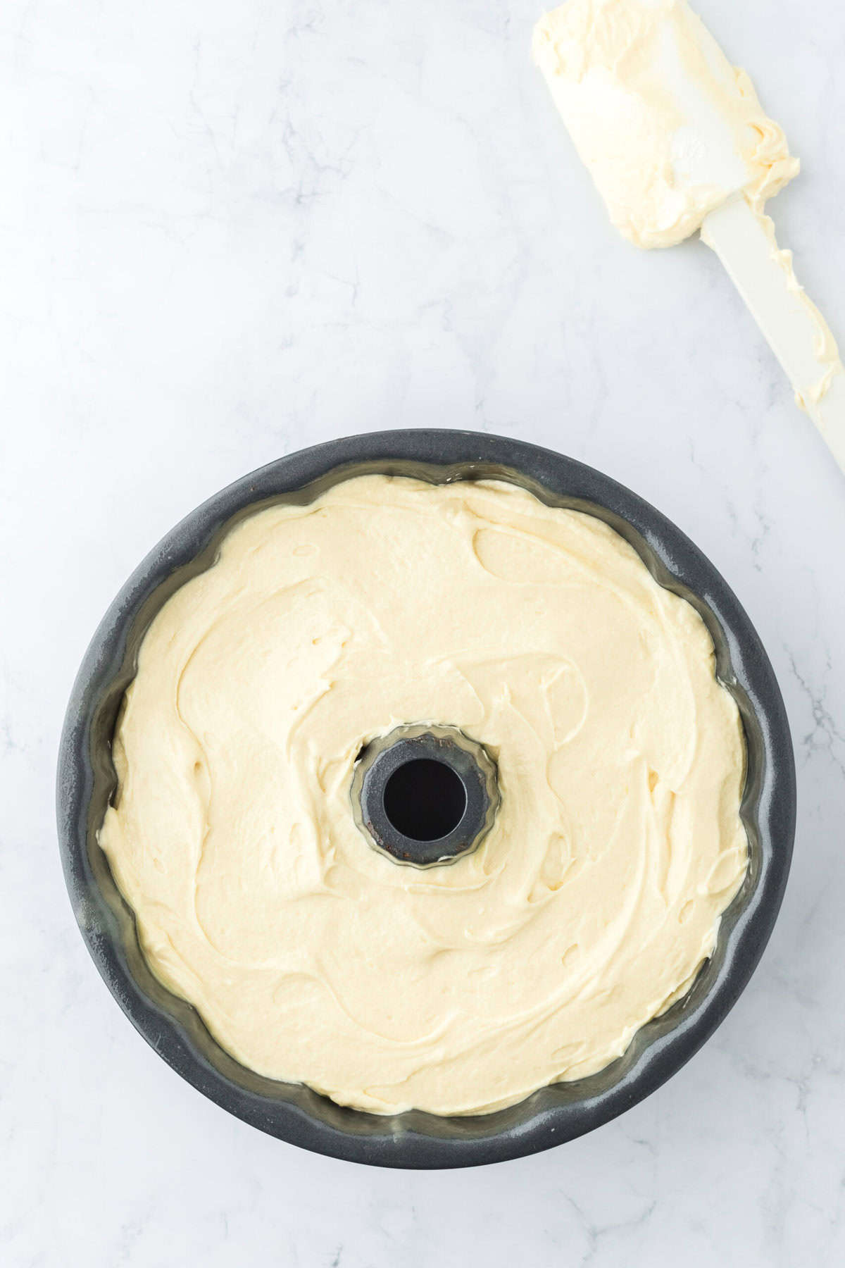 Cake batter poured into a bundt pan before baking on white countertop